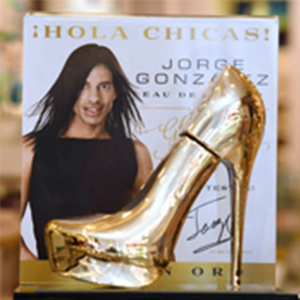Jorge González with a golden high heel and a perfume bottle