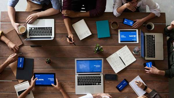 Acht Menschen an einem großen Tisch mit Laptops