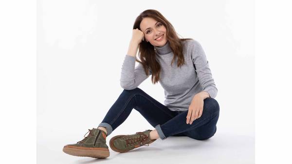 Sitzendes Model in grauem Shirt, blauer Hose und grünen Schuhen