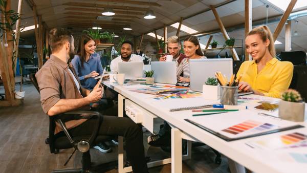 Creative team at a long white desk with laptops, colour swatches and sketches in an open office.