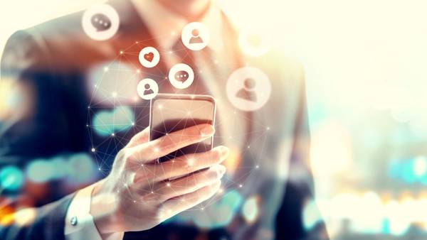 Hand holding a smartphone with floating message and profile icons above it.