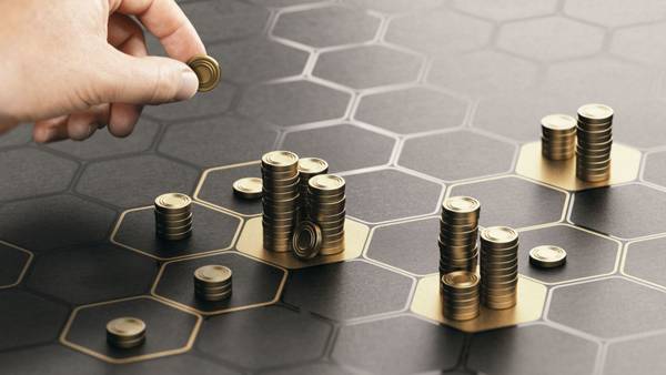 Hand placing a coin on a honeycomb pattern with stacks of coins of different heights.