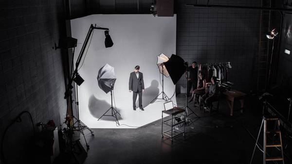 Photo studio with a white cyclorama, softboxes and a man in a suit in front of the camera.