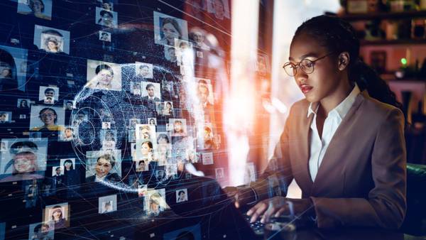 Woman at a laptop in front of a globe made of many small profile pictures.