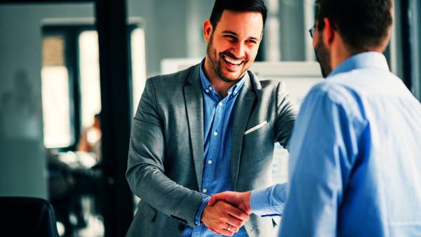Two men shaking hands and smiling in an office.