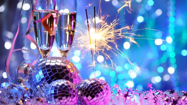 Champagne glasses, a sparkler and disco balls against blue and turquoise bokeh.