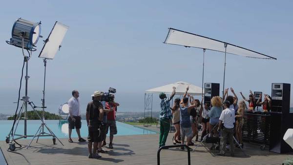Film set by a pool with lamps, reflectors and a group with raised arms.